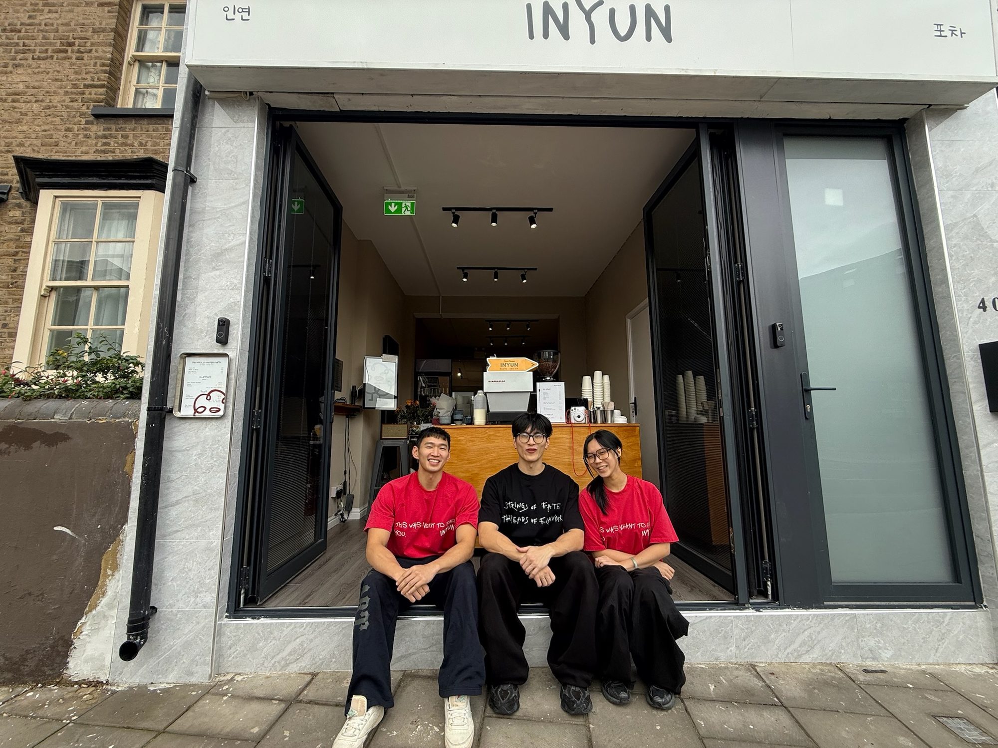 INYUN's three founders sitting together in the shopfront doorway under the hand-drawn sign